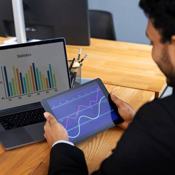 A person analyzing graphs on a tablet and laptop at a desk A person analyzing graphs on a tablet and laptop at a desk